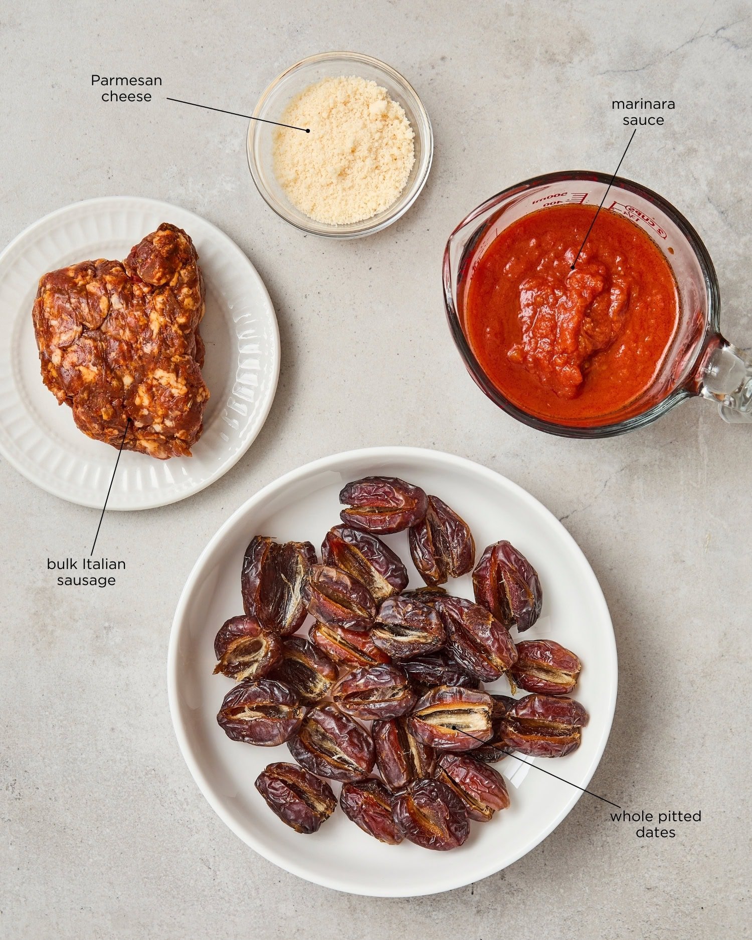 Concrete surface with ingredients needed for stuffed dates including marinara sauce, sausage, and Parmesan.