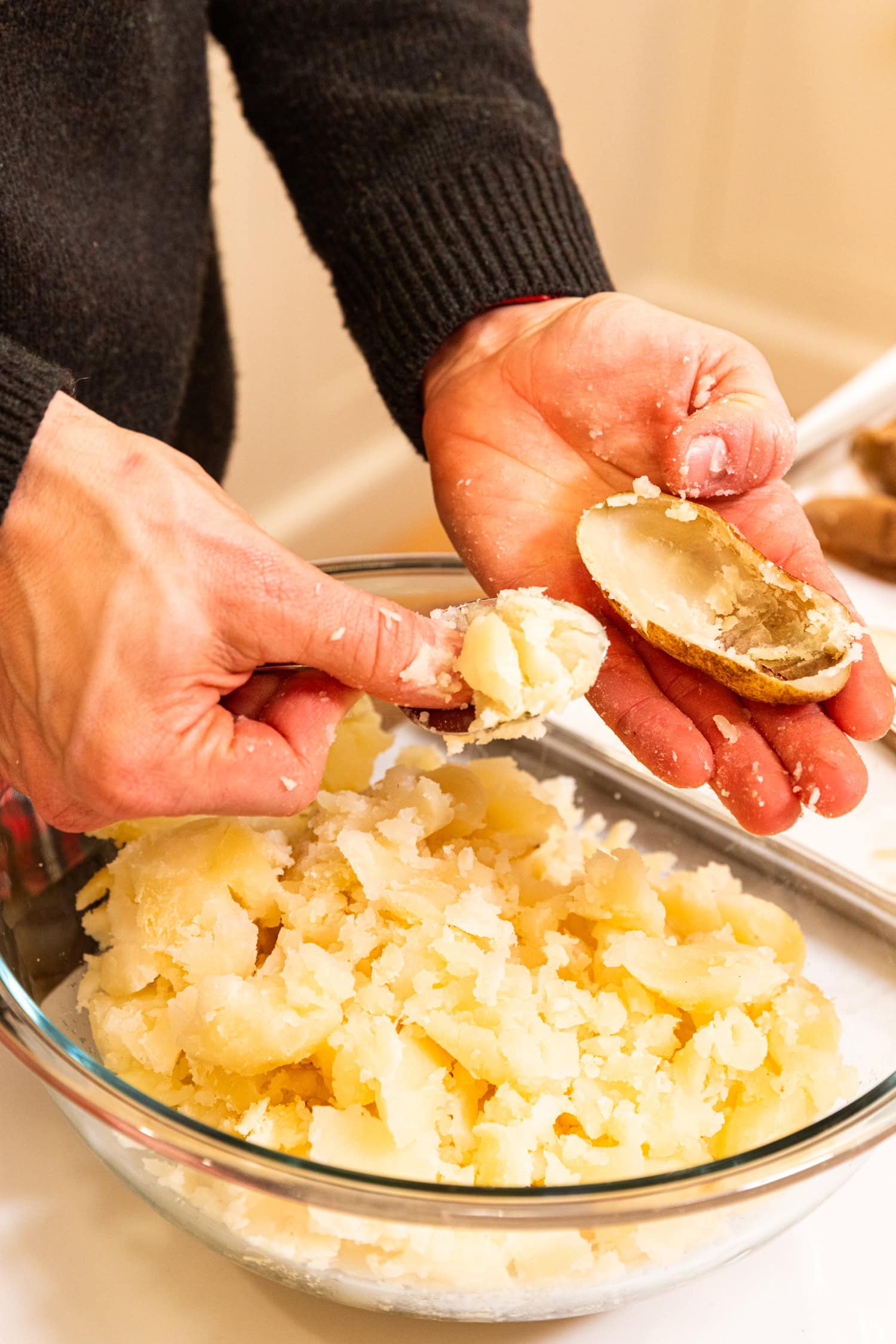Hand scooping out baked interior of a potato into a bowl.