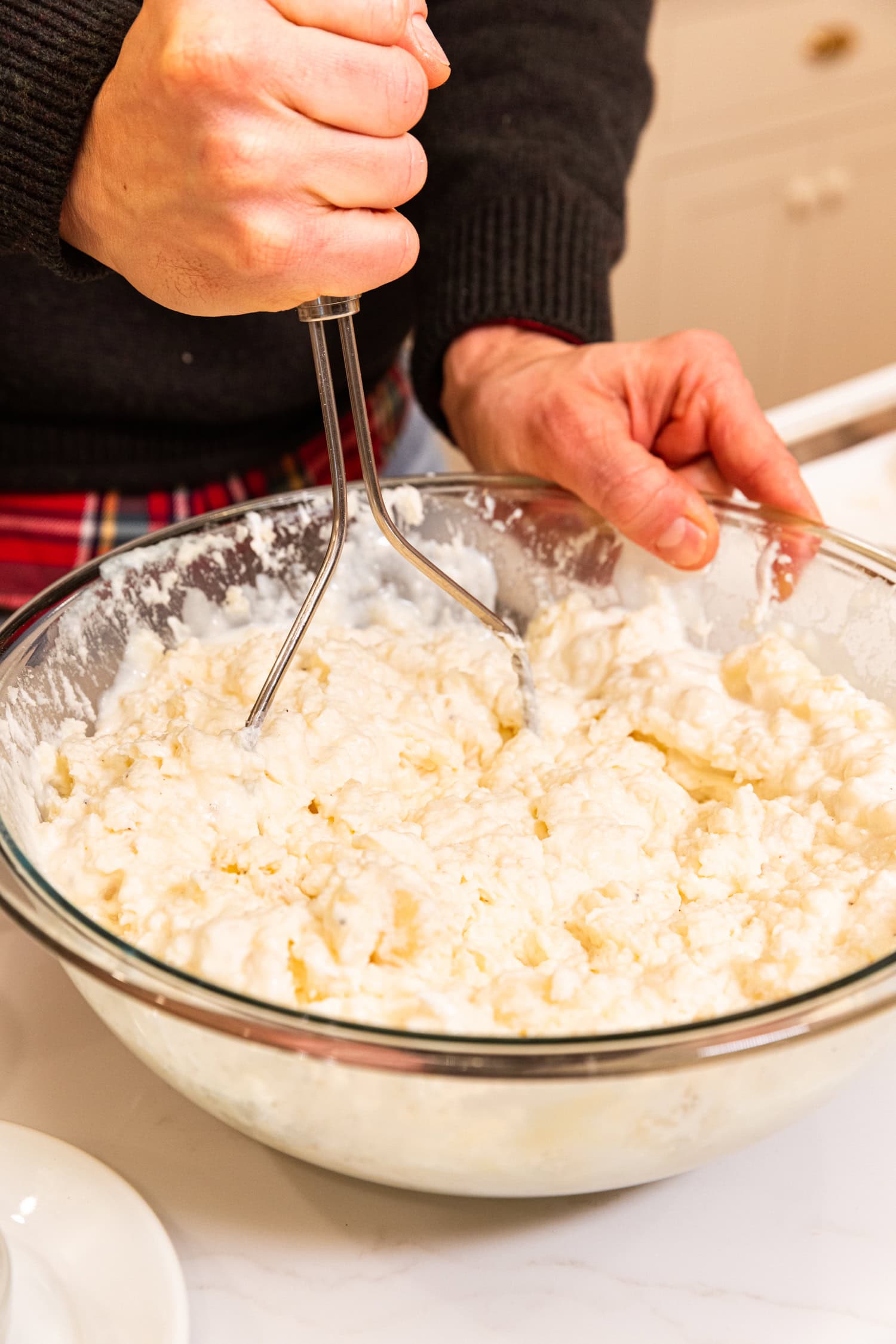 Hand mashing potatoes in a large bowl with other liquids.