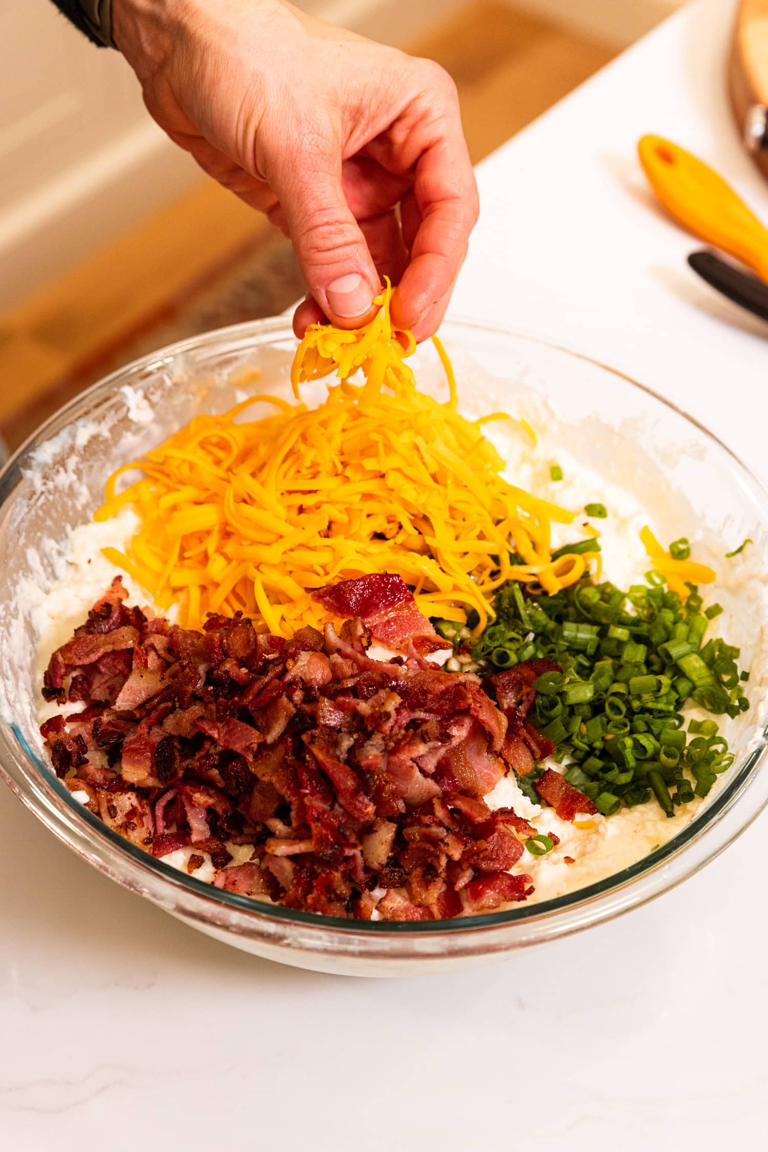 Bowl with mashed potatoes underneath piled with cooked bacon, scallions, and cheese.