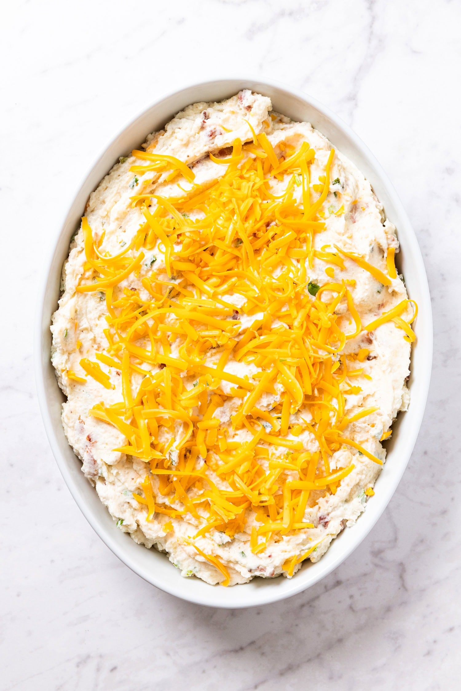 Unbaked twice-baked potato casserole with shredded cheese on top,.