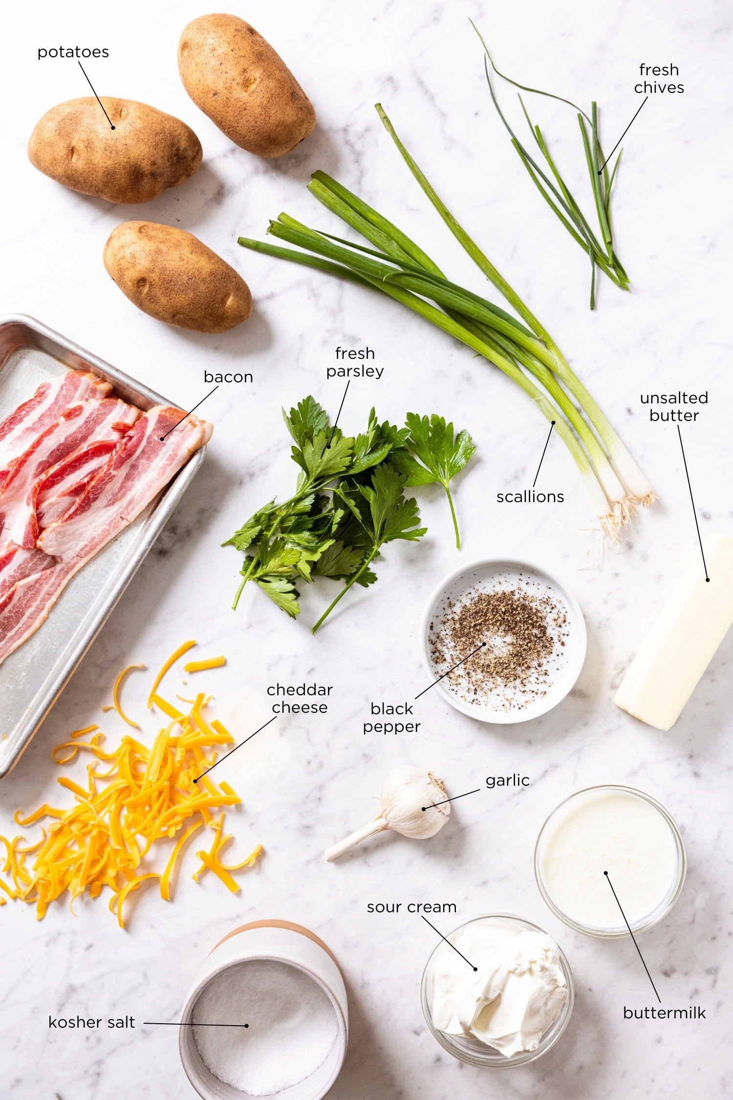 White marble surface with ingredients needed for twice-baked potato casserole including bacon, potatoes, cheese, and more.