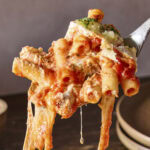 Spoonful of baked ziti with cheese pull handing below showing pasta.