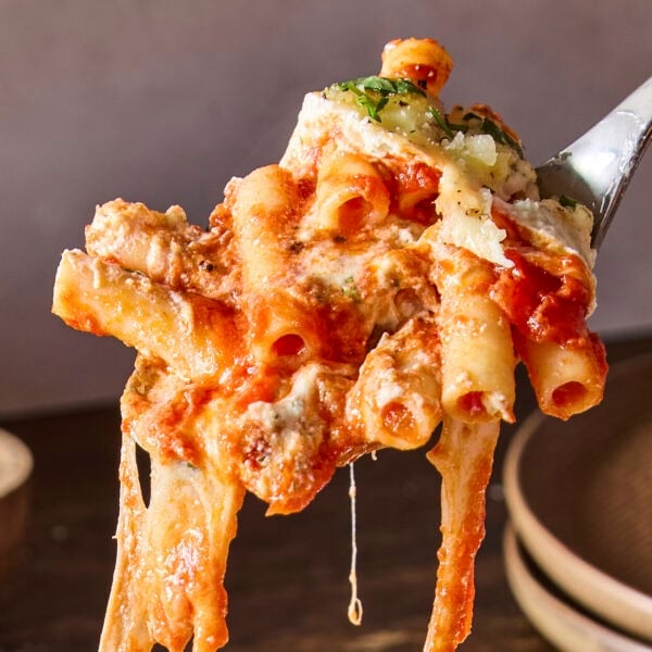 Spoonful of baked ziti with cheese pull handing below showing pasta.