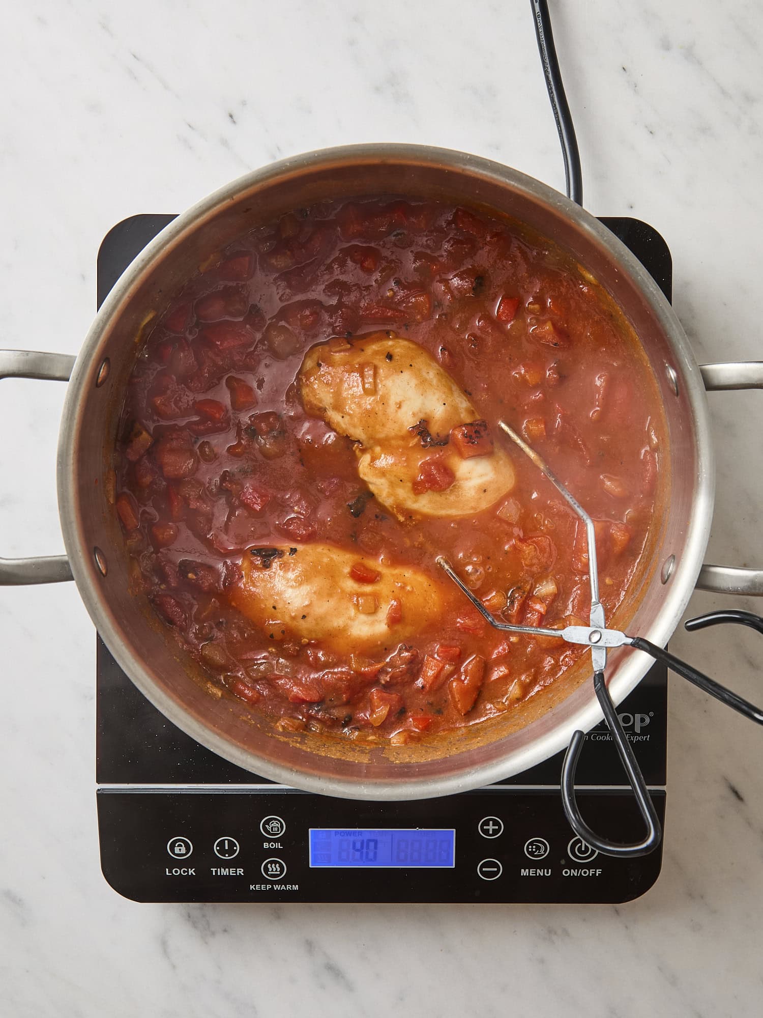 Pot cooking with tomatoes and chicken poaching inside.