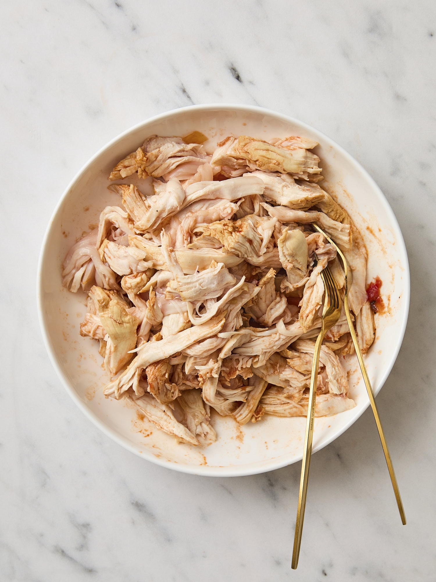 White bowl filled with poached shredded chicken.