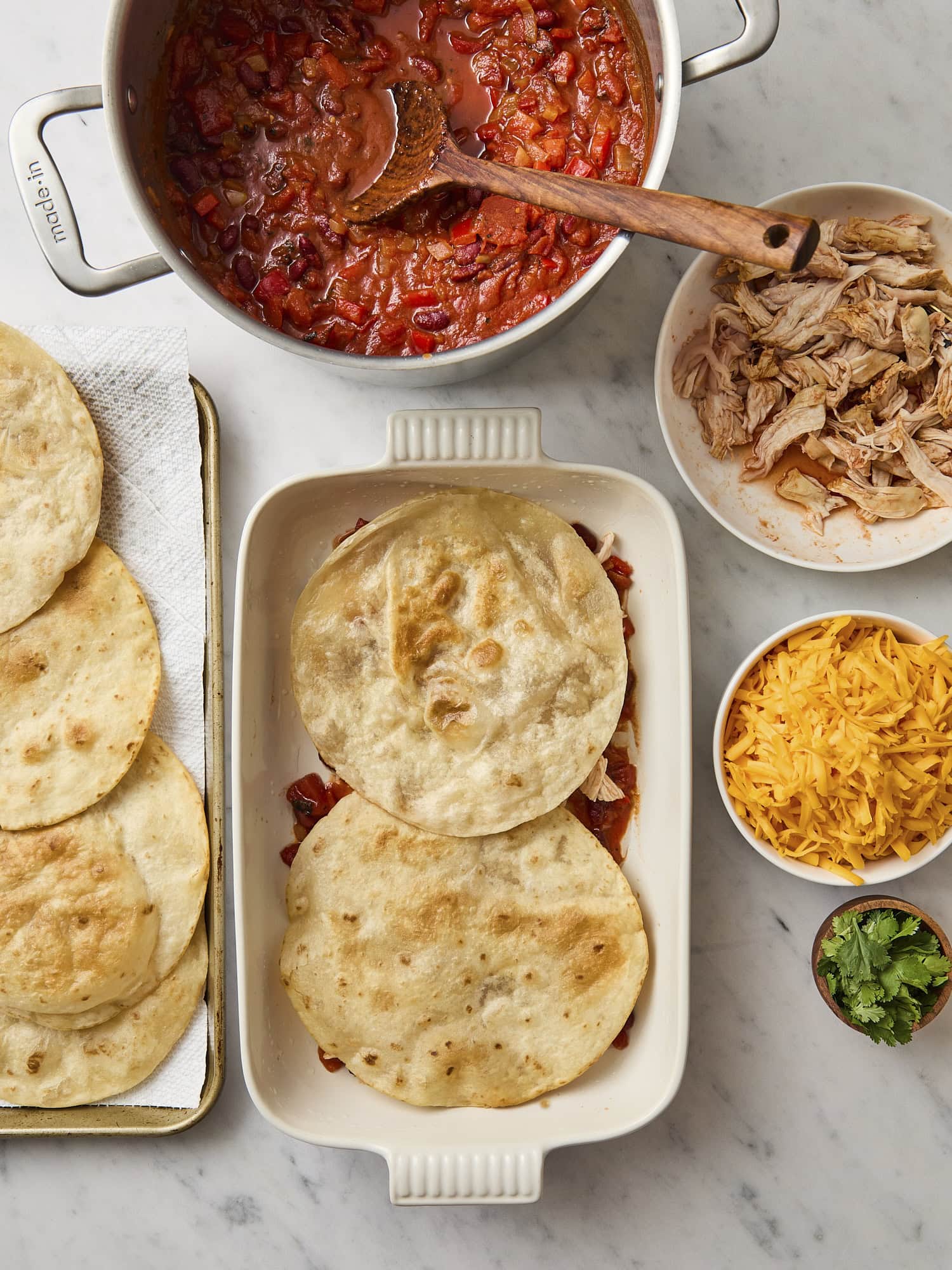 Flour tortillas on top of sauce in a white baking dish.