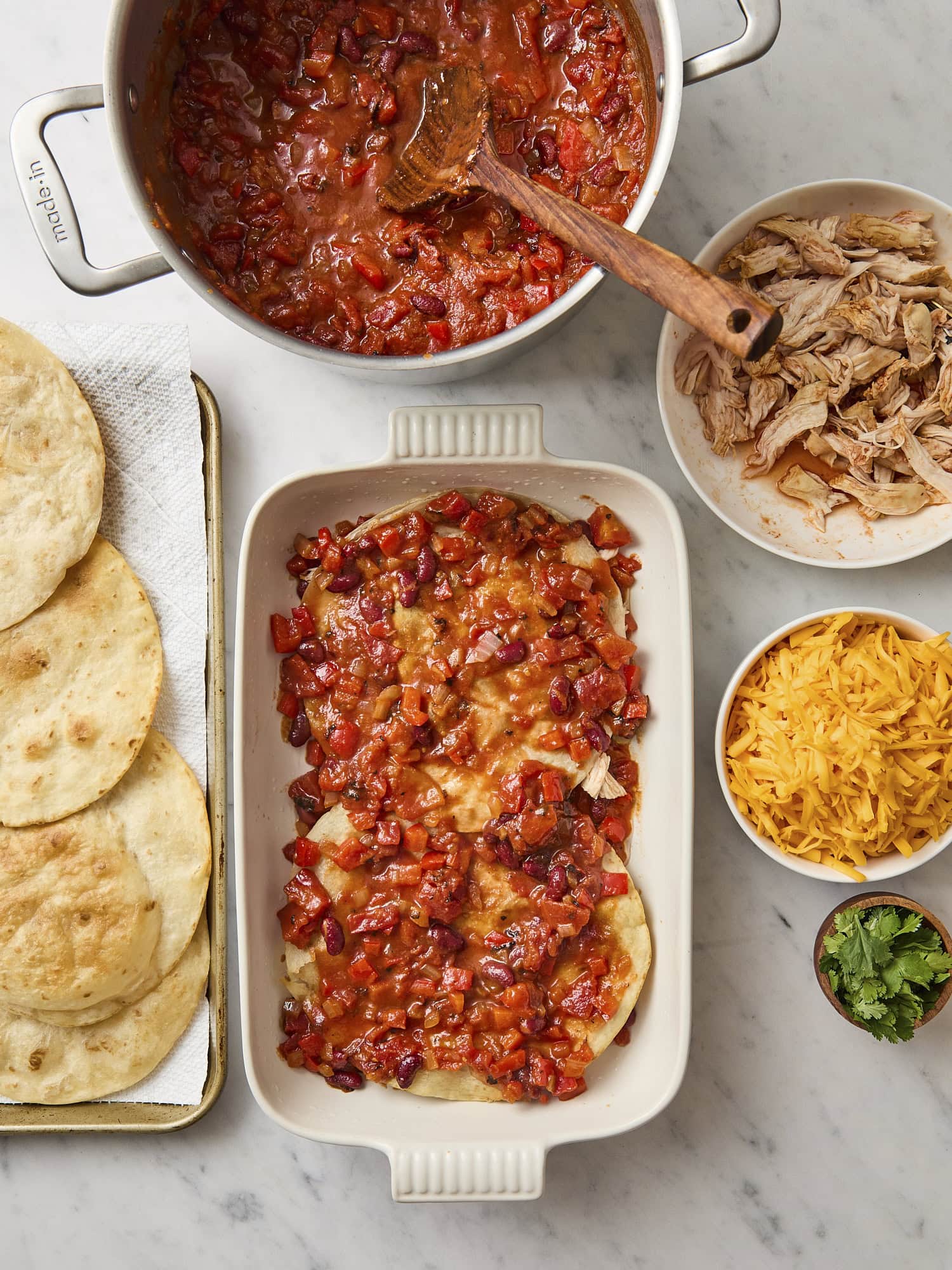 Tomato sauce on top of flour tortillas assembling chicken tortilla casserole.