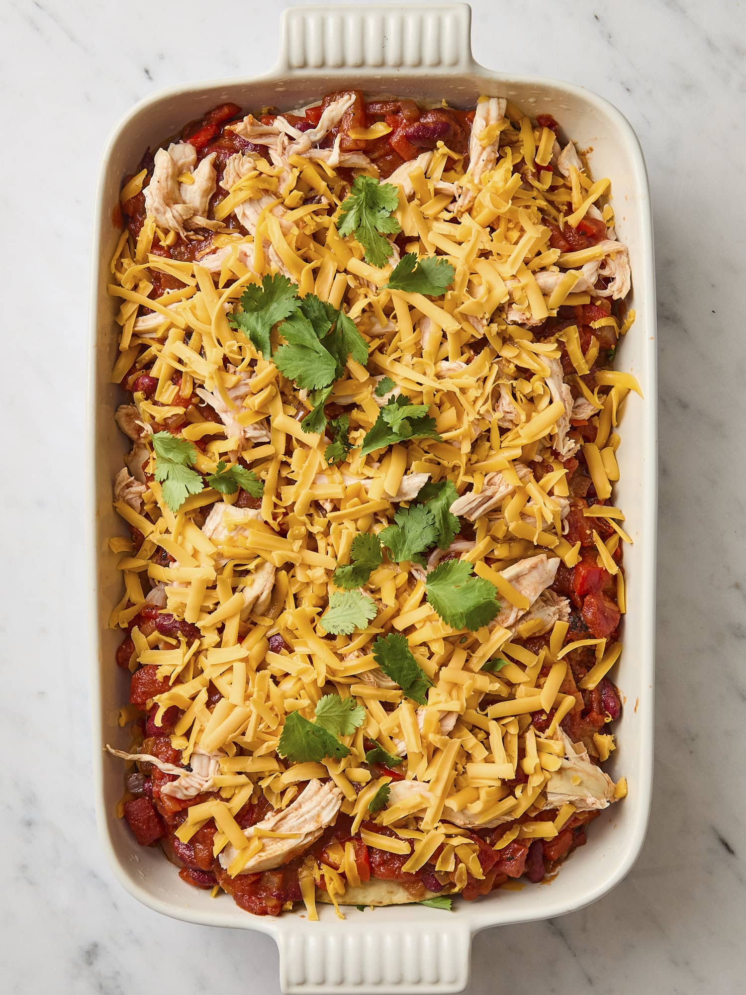 Unbaked chicken tortilla casserole with cilantro and cheese sprinkled on top.