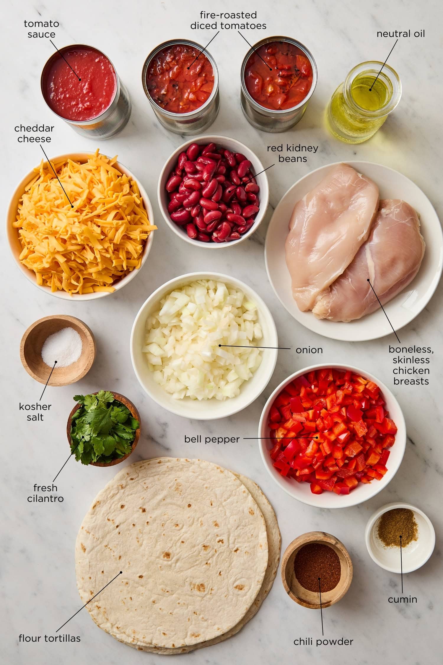 Marble surface with ingredients needed for chicken tortilla casserole including tortillas, chicken, cheese, and veggies.