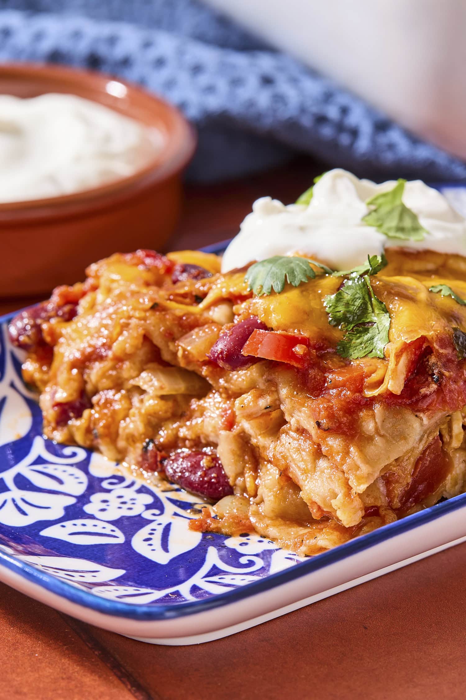 Serving of chicken tortilla casserole on a patterned plate with dollop of sour cream on top.