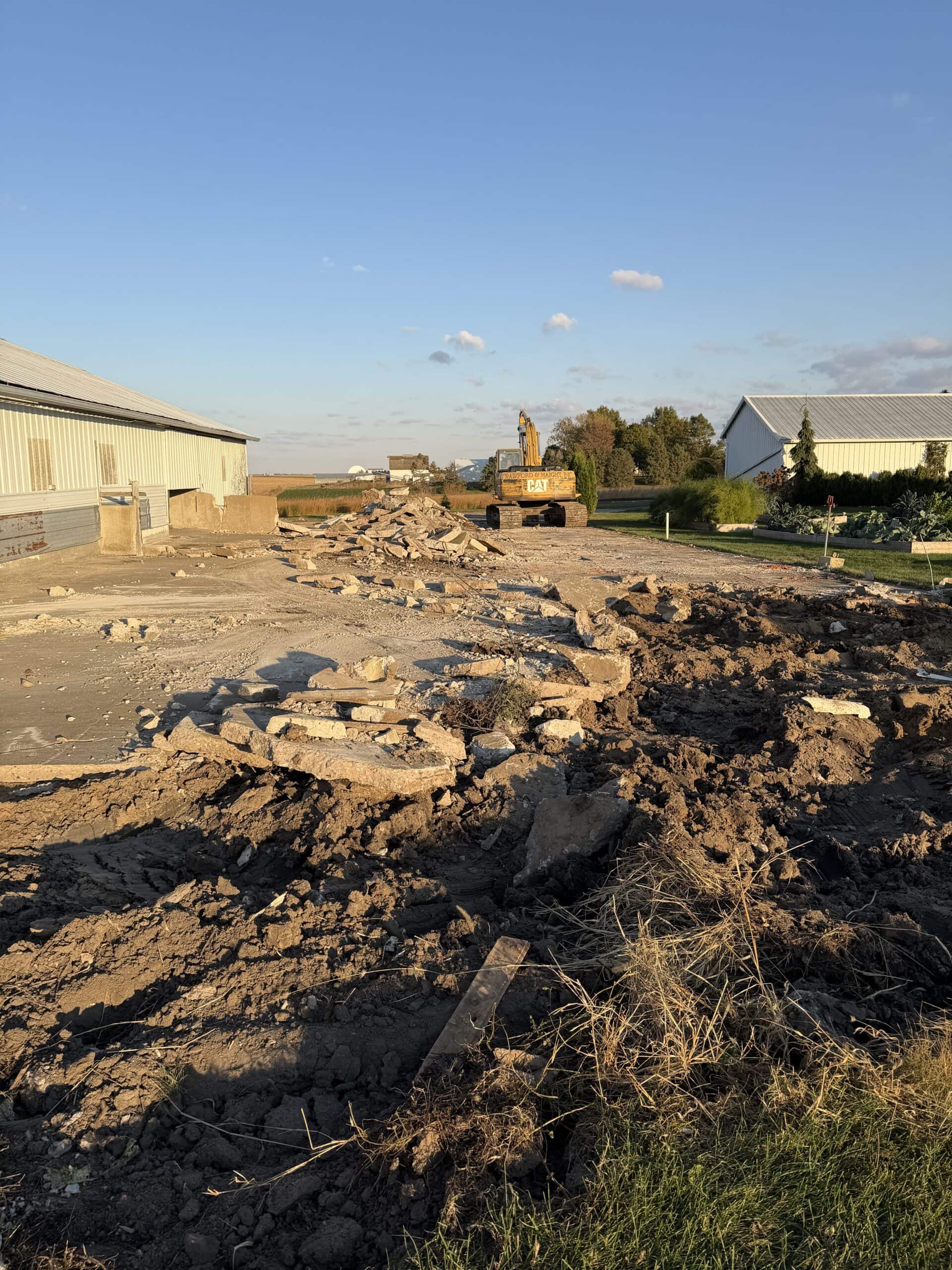 Farm building with concrete being removed in front with machinery in background.