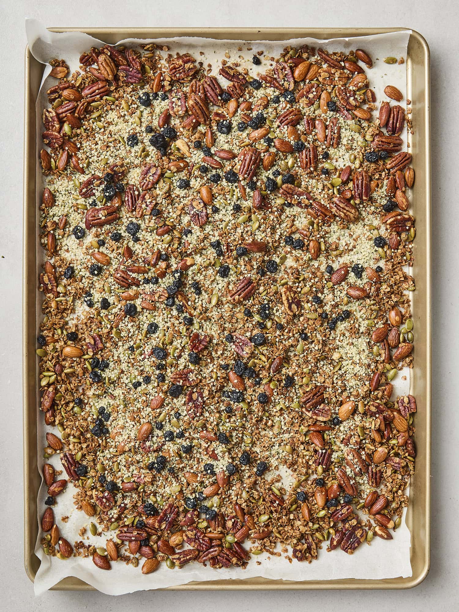 Sheet pan with baked granola with hemp hearts and blueberries sprinkled on top.