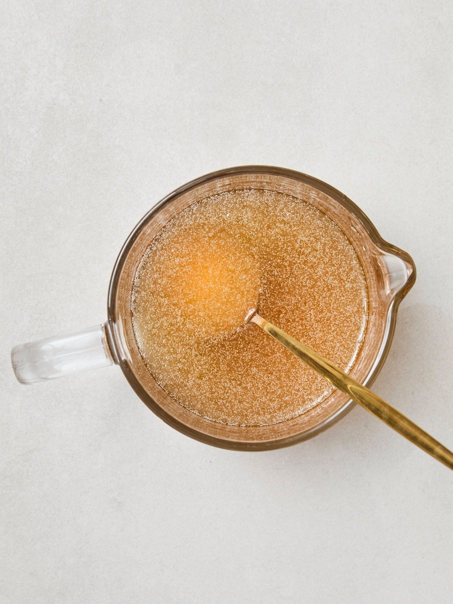 Glass measuring cup filled with melted coconut oil, maple syrup, and honey for granola.