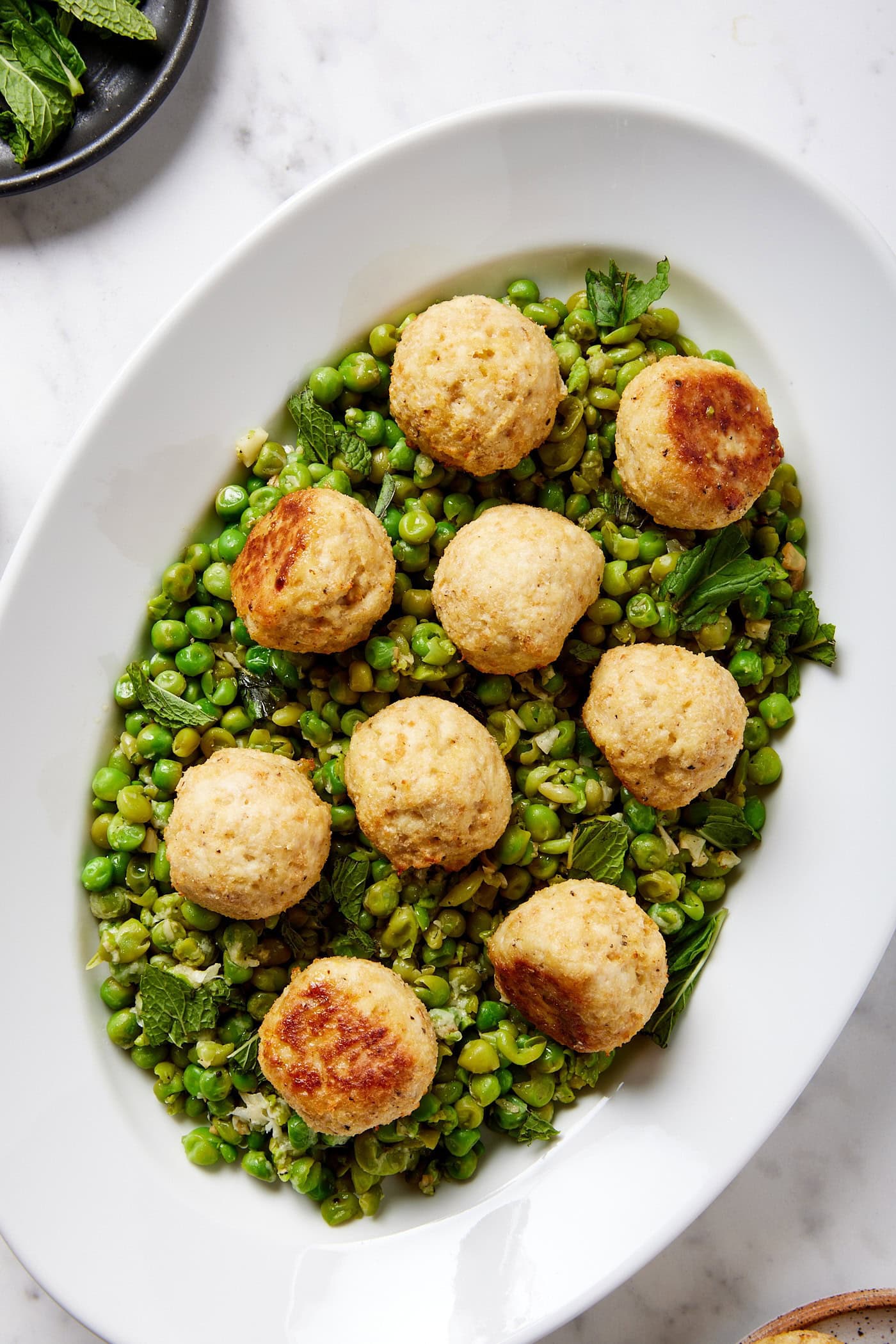 Plate filled with baked chicken meatballs with a pea mash underneath.