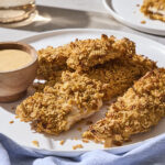 Chicken strips with crispy coating on plate with honey mustard sauce.