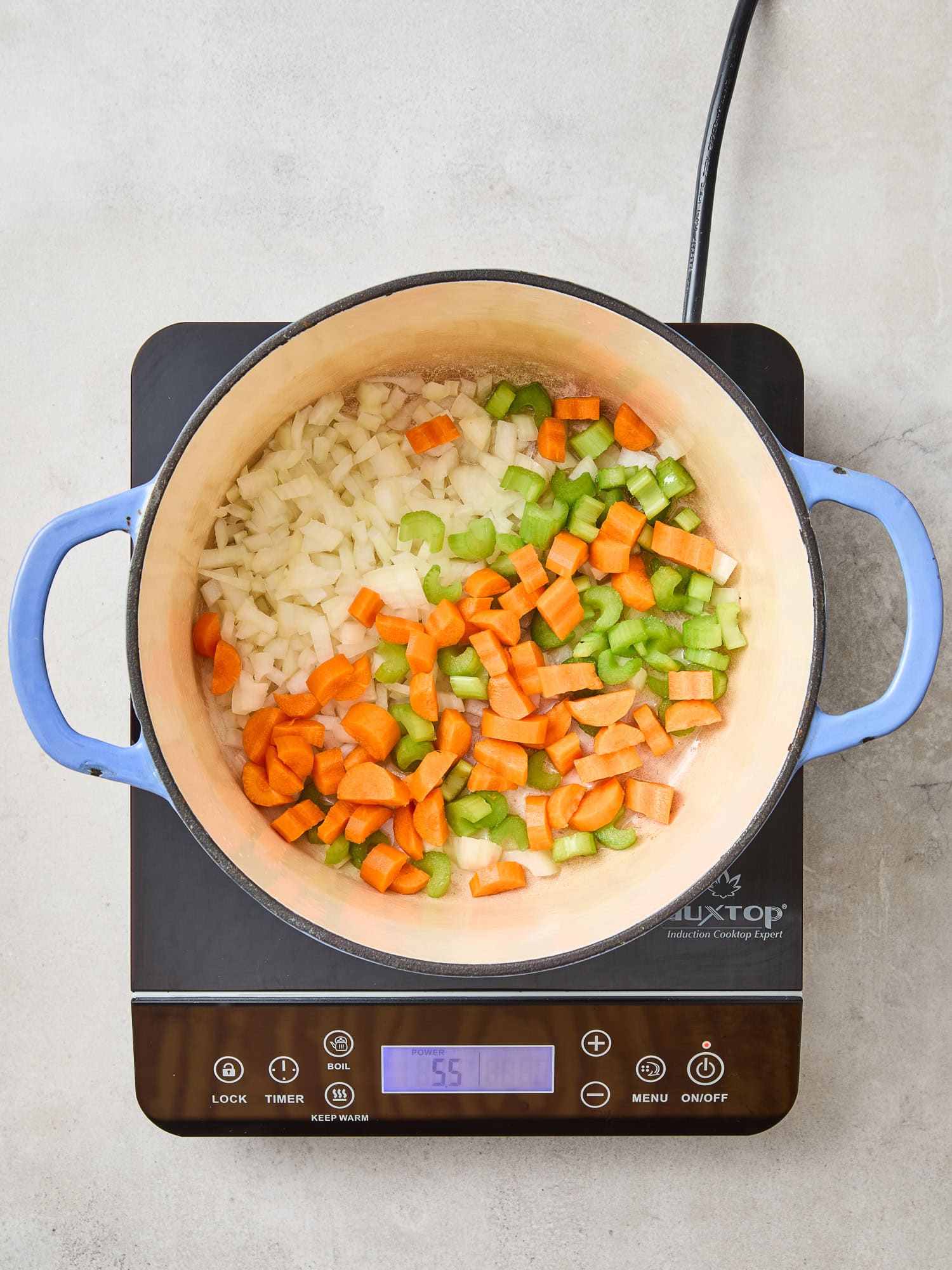 Onion, celery, and carrot sautée over a cooktop.