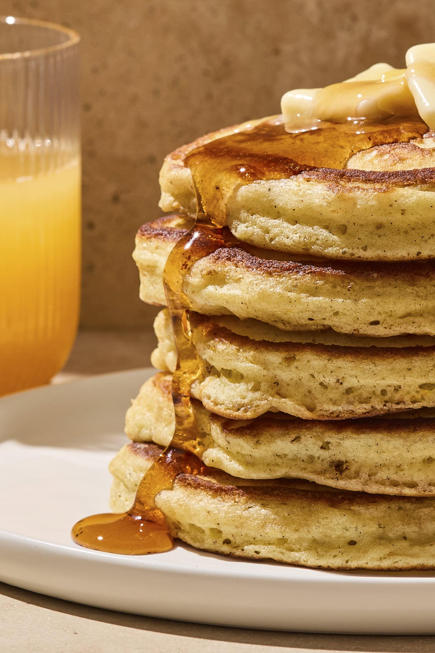 Stack of buttermilk pancakes with syrup dripping down the side.