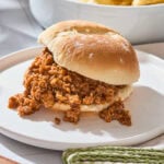 A hamburger bun with sloppy joe meat rests on a plate.