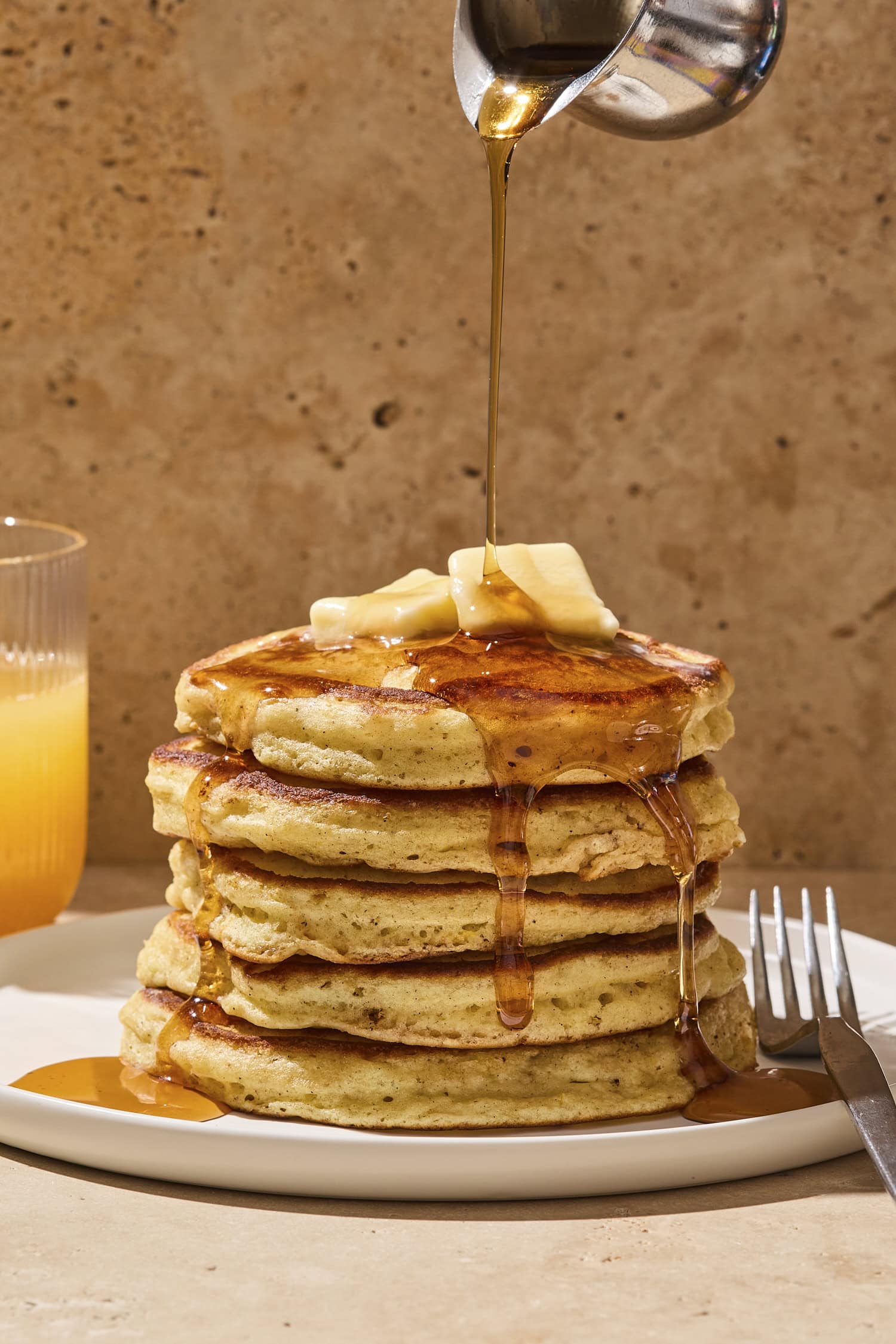Syrup being drizzled on top of a stack of pancakes with butter.