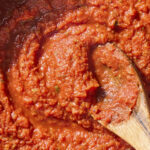 Wooden spoon stirring together easy marinara sauce in a pan.
