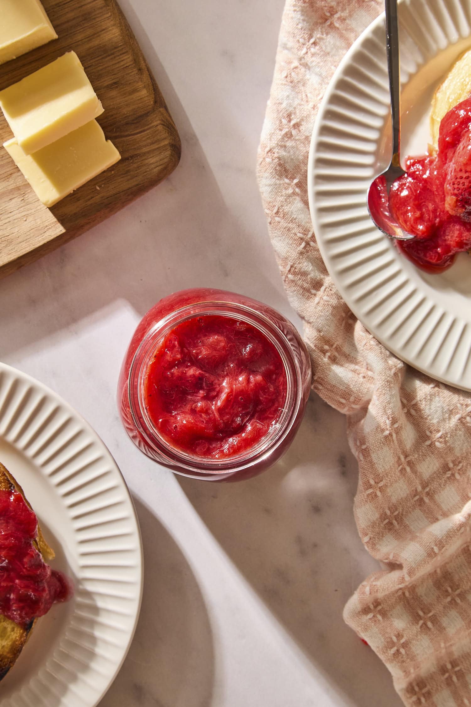 Jar on countertop with rhubarb sauce with plates and butter.