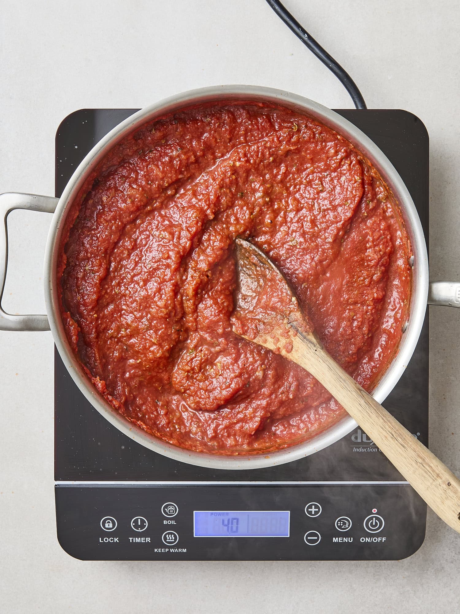 Marinara sauce cooking in a saucepan with a wooden spoon stirring.