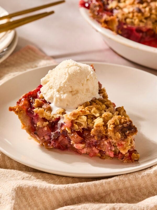 Piece of rhubarb pie on a plate with a scoop of ice cream on top.
