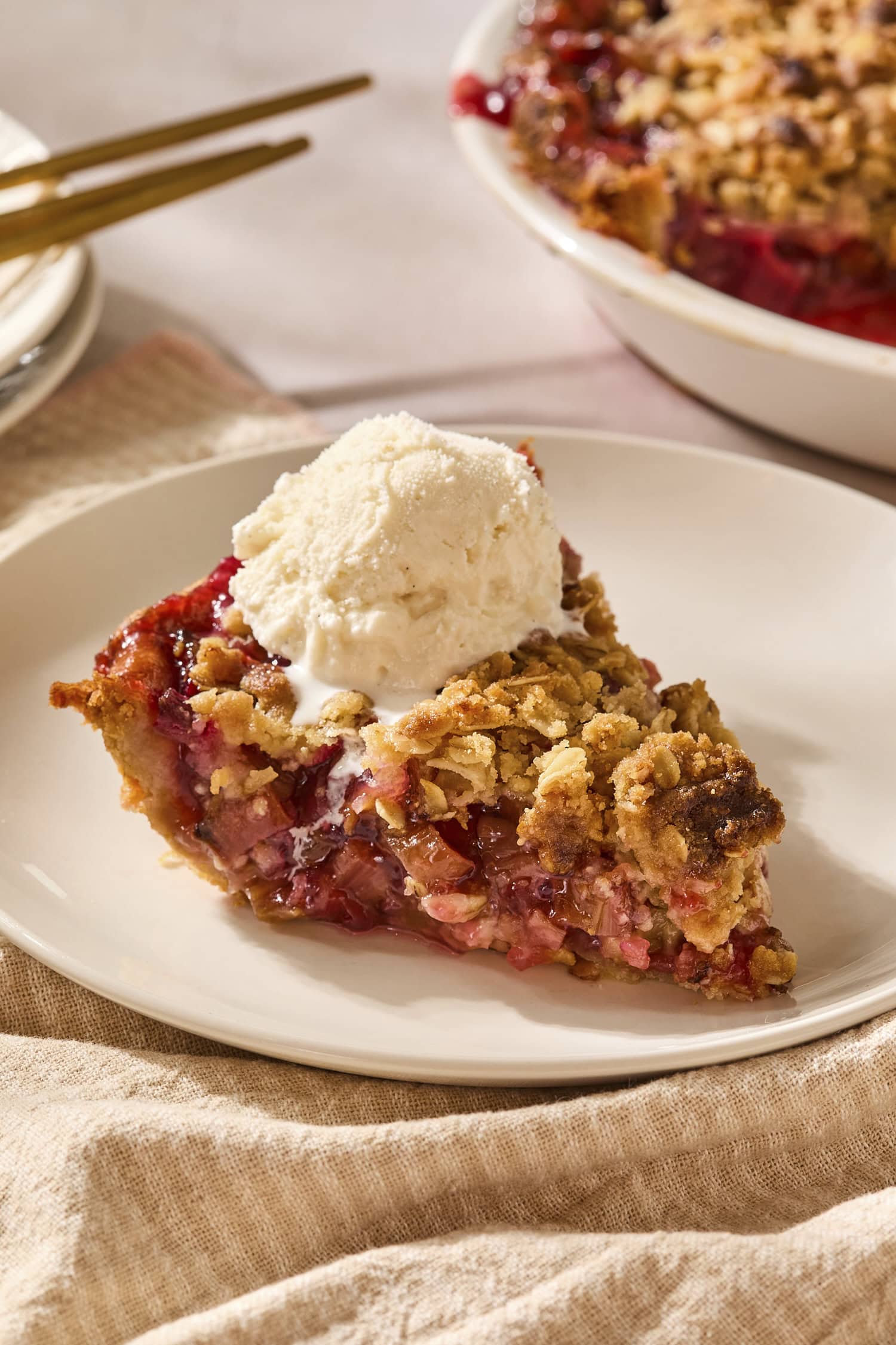 Piece of rhubarb pie on a plate with a scoop of ice cream on top.