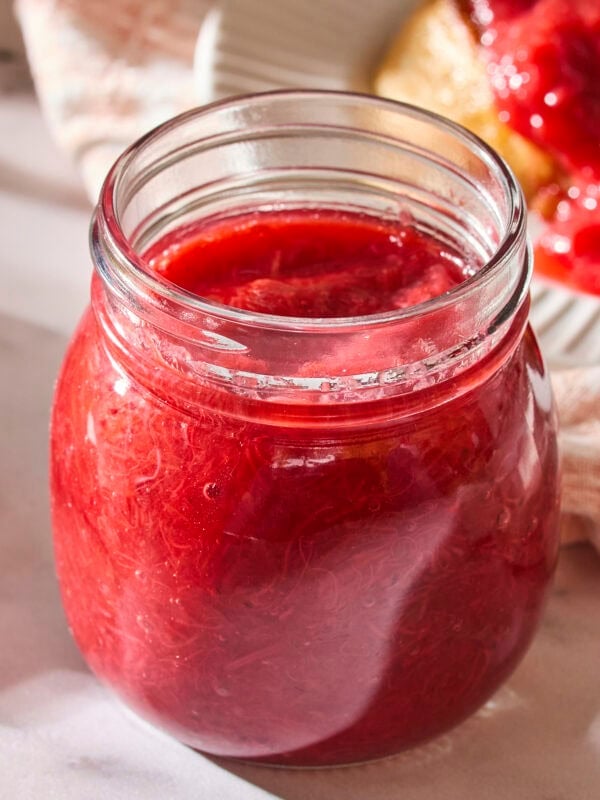 Jar filled with red-colored strawberry rhubarb sauce.