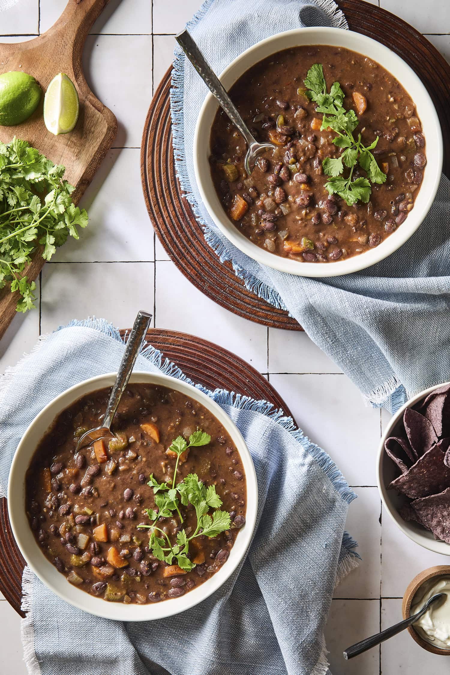 A table with two servings of black bean soup and a side of sour cream and tortilla chips.