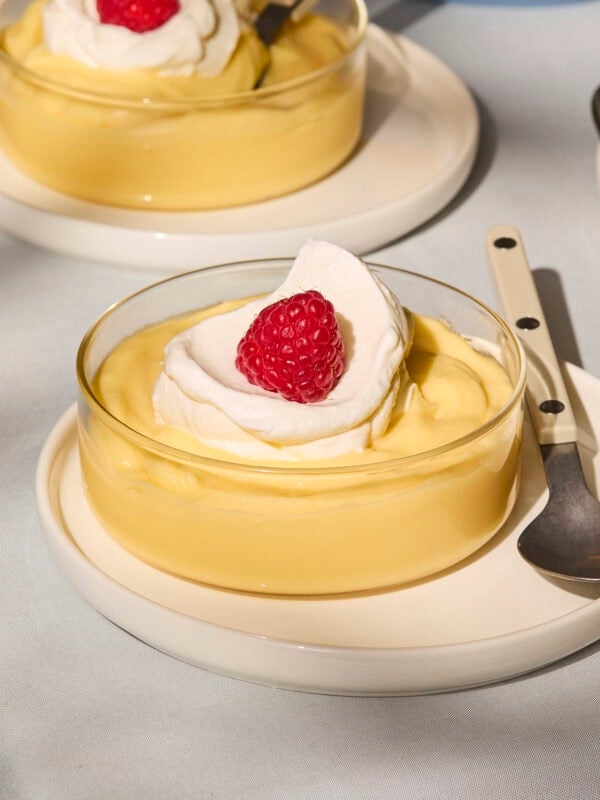 Glass of lemon pudding with whipped cream and raspberry on top.