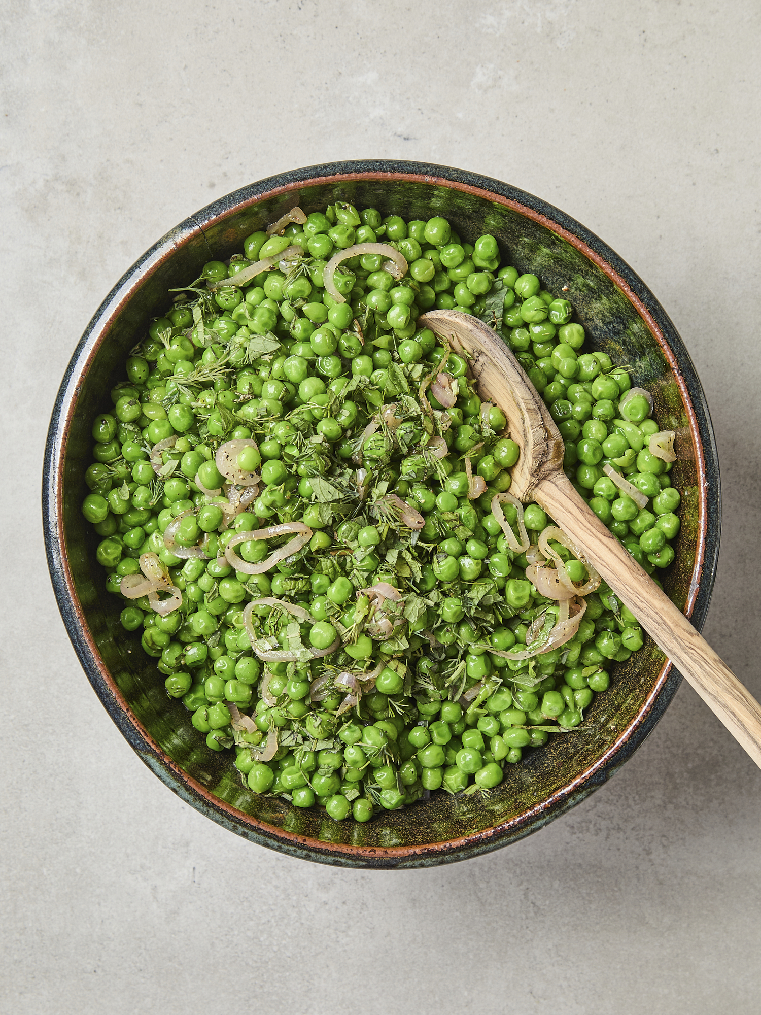 Lemon herb peas with serving spoon and fresh herbs on top.