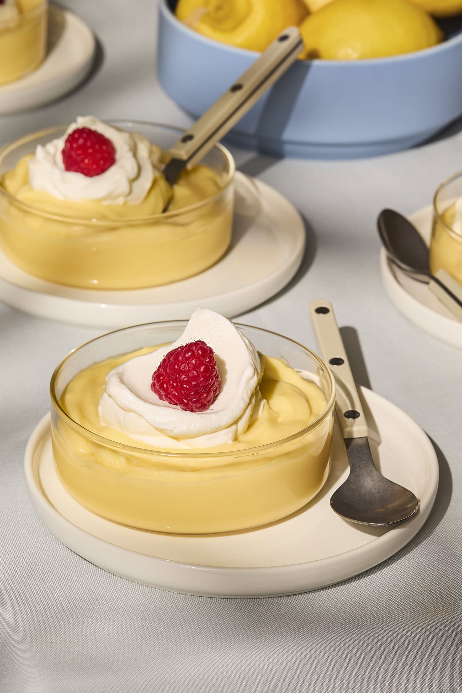 Two glasses filled with lemon pudding with whipped cream and raspberry on top.