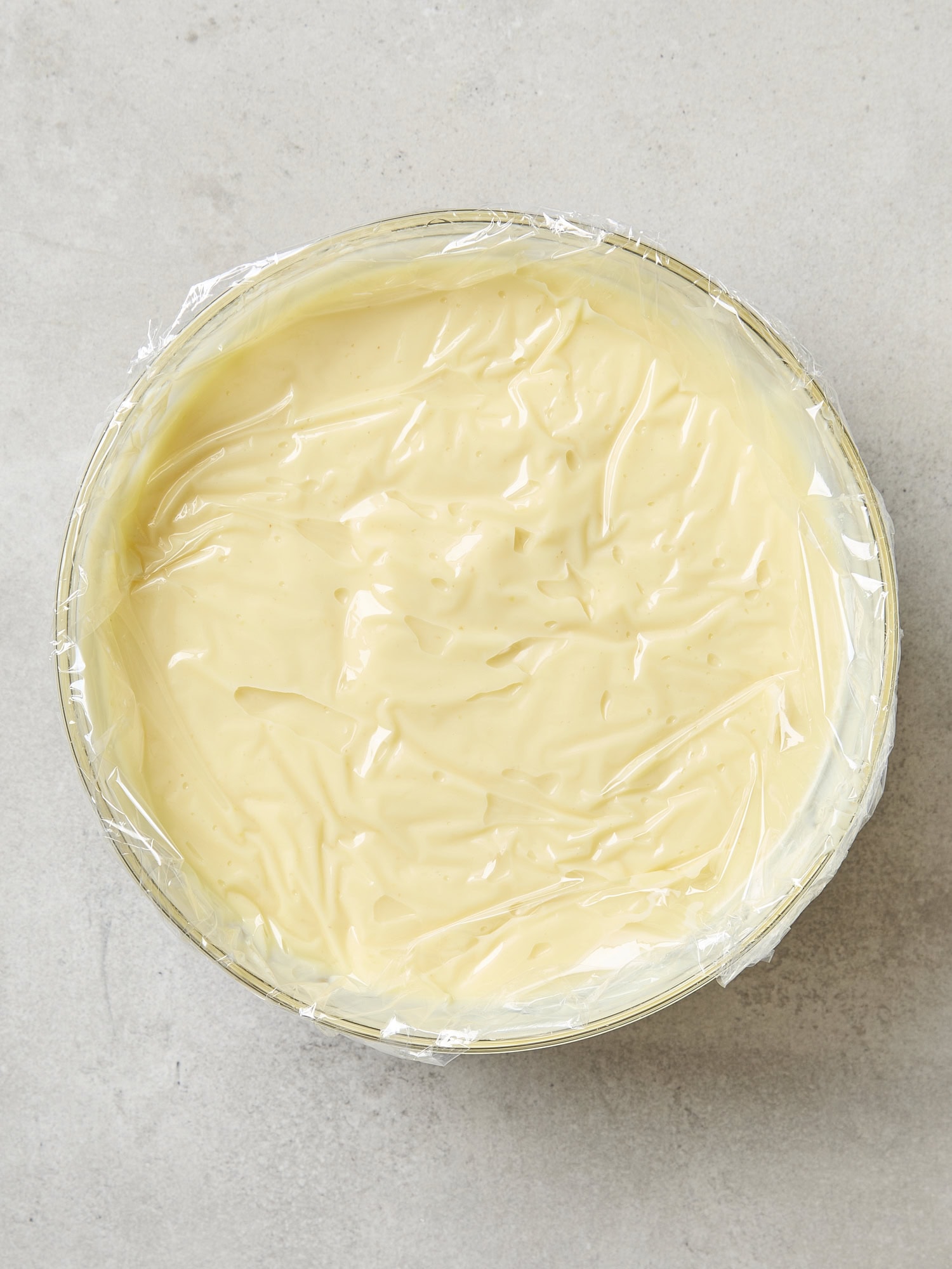 Plastic wrap on top of lemon pudding in glass bowl.