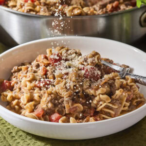 Parmesan cheese being sprinkled over the top of a serving of beef ragu pasta.