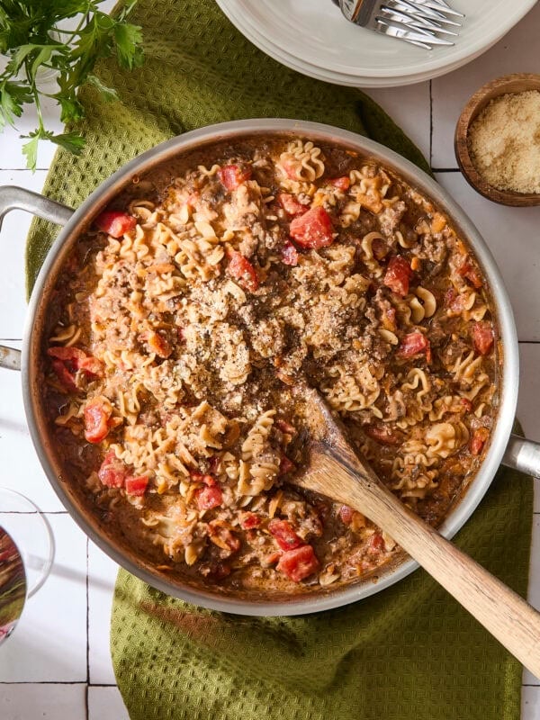 Skillet of beef ragu with wooden spoon scooping up a serving.