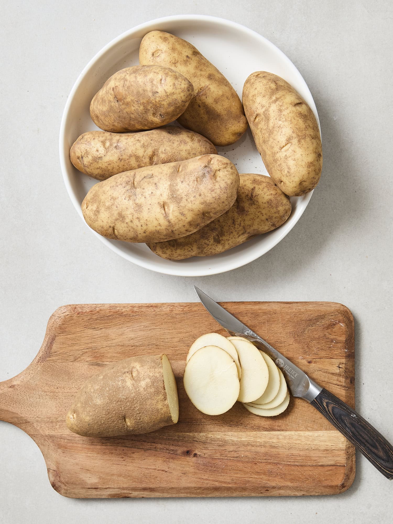 Slicing russet potatoes on cutting board.