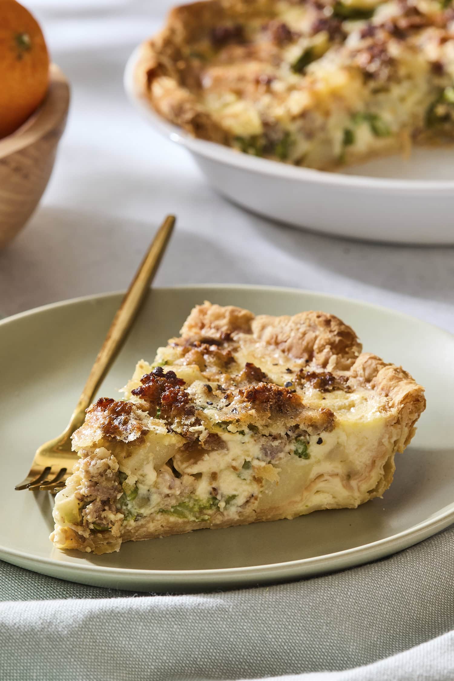 Slice of sausage asparagus quiche on a plate with rest in background.
