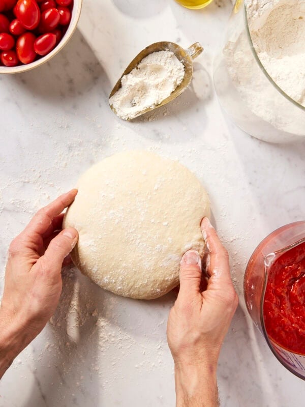 Two hands rolling up pizza dough recipe.