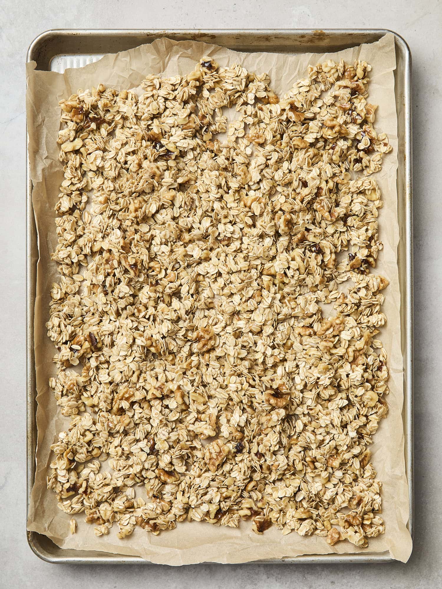 Oatmeal and walnut granola spread out on baking sheet before being baked.