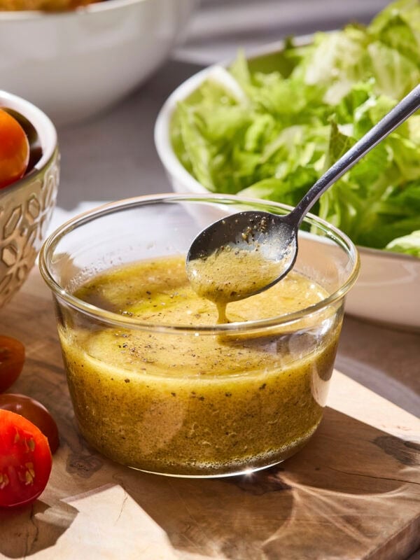 Spoon scooping up Dijon vinaigrette from glass jar.