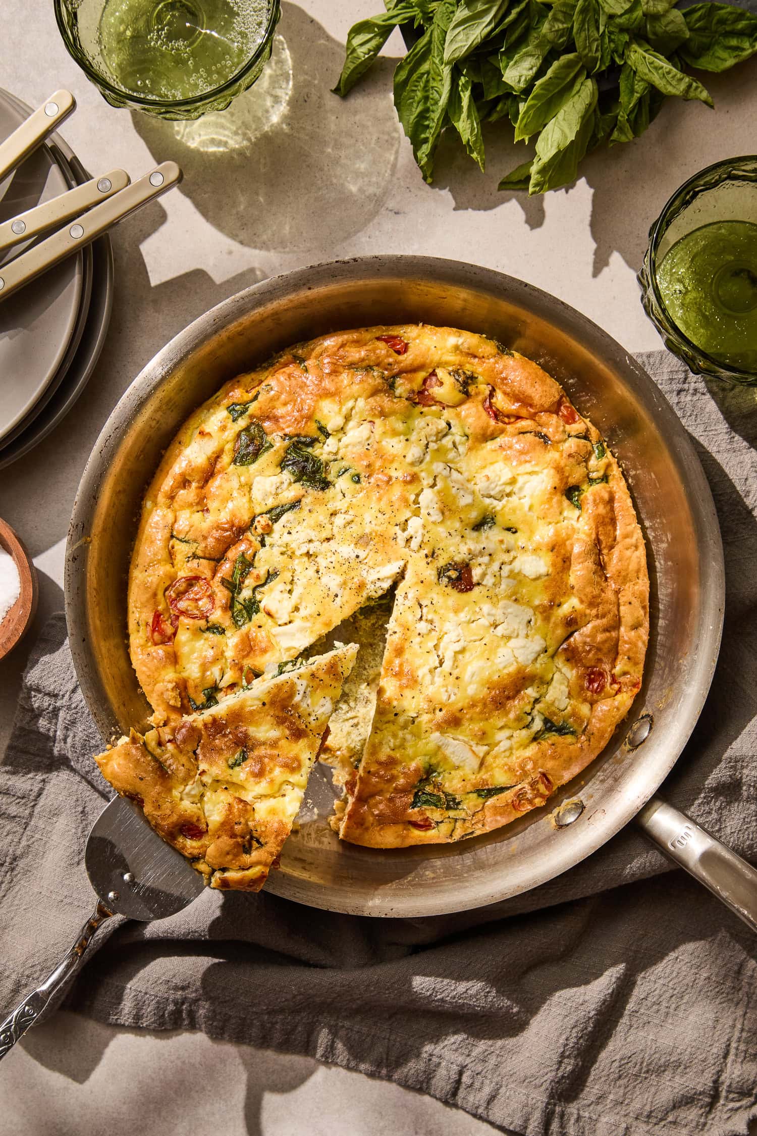 Removing a wedge of tomato spinach frittata from the pan.