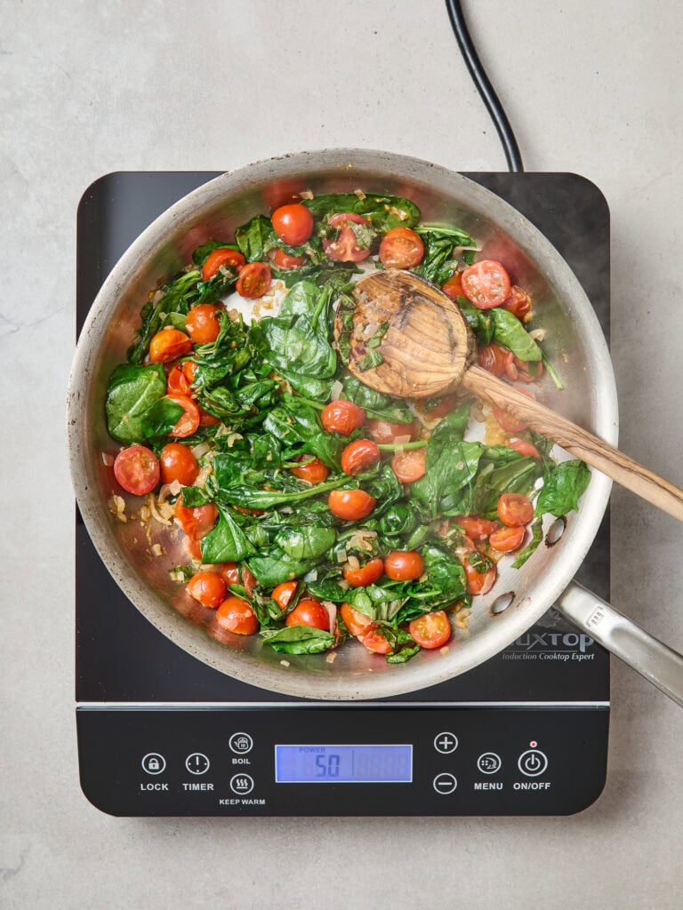 Cooking spinach and tomatoes in a skillet for a frittata.