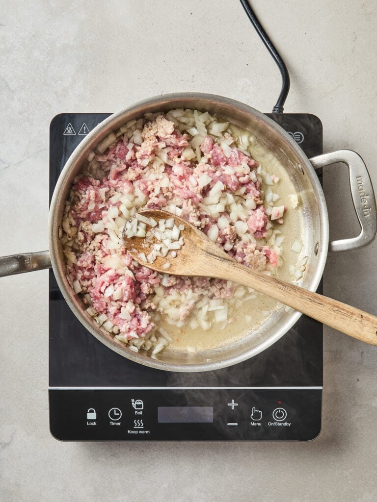 Onion, garlic, and pork cook in a skillet.