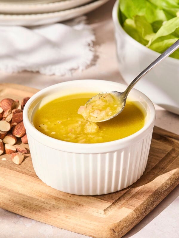 Spoon picking up some vinaigrette in a small white bowl.