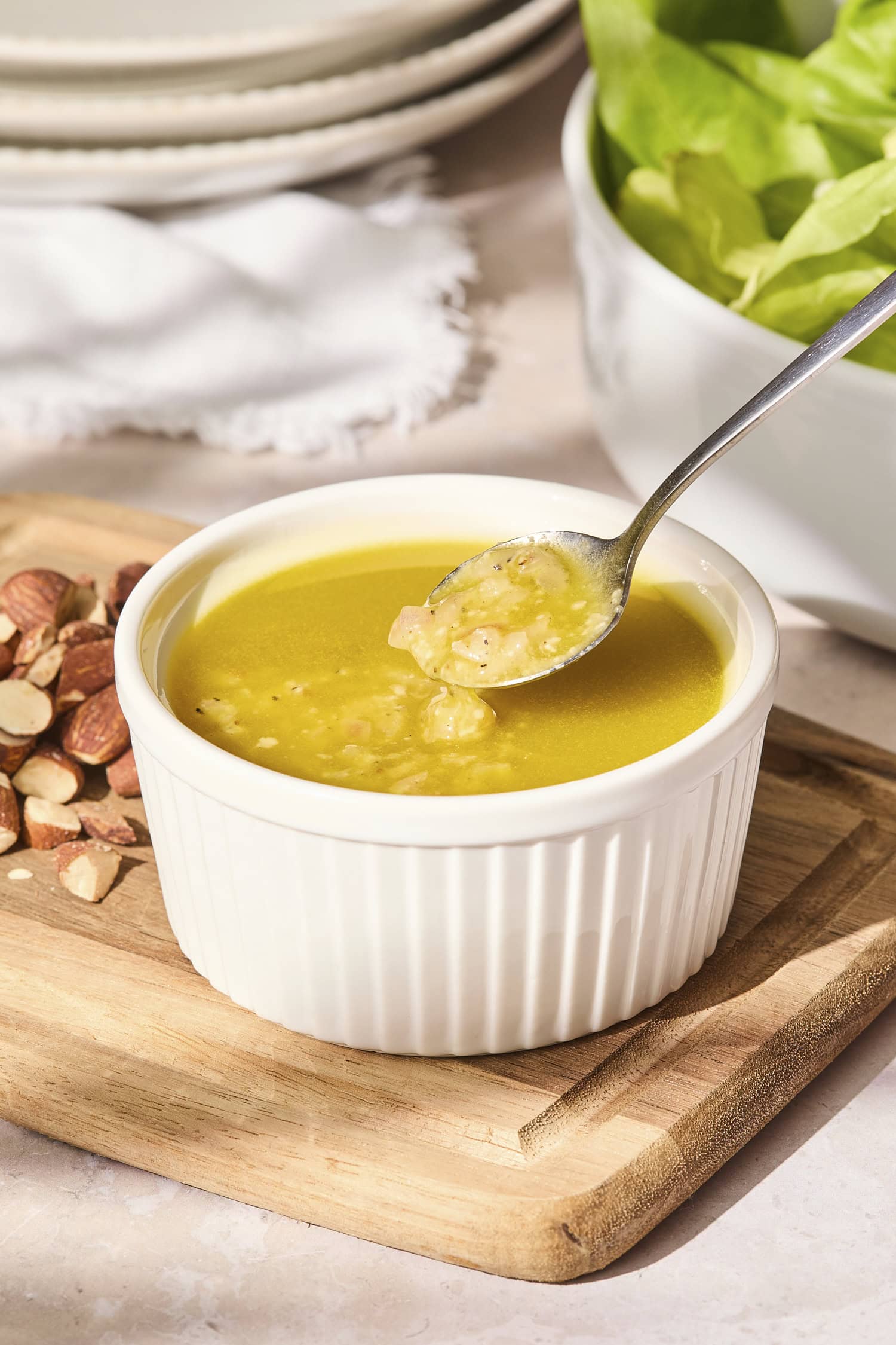 Spoon picking up some vinaigrette in a small white bowl.