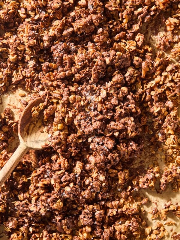 Spoon mixing pieces of chocolate chip cookie granola on baking sheet.