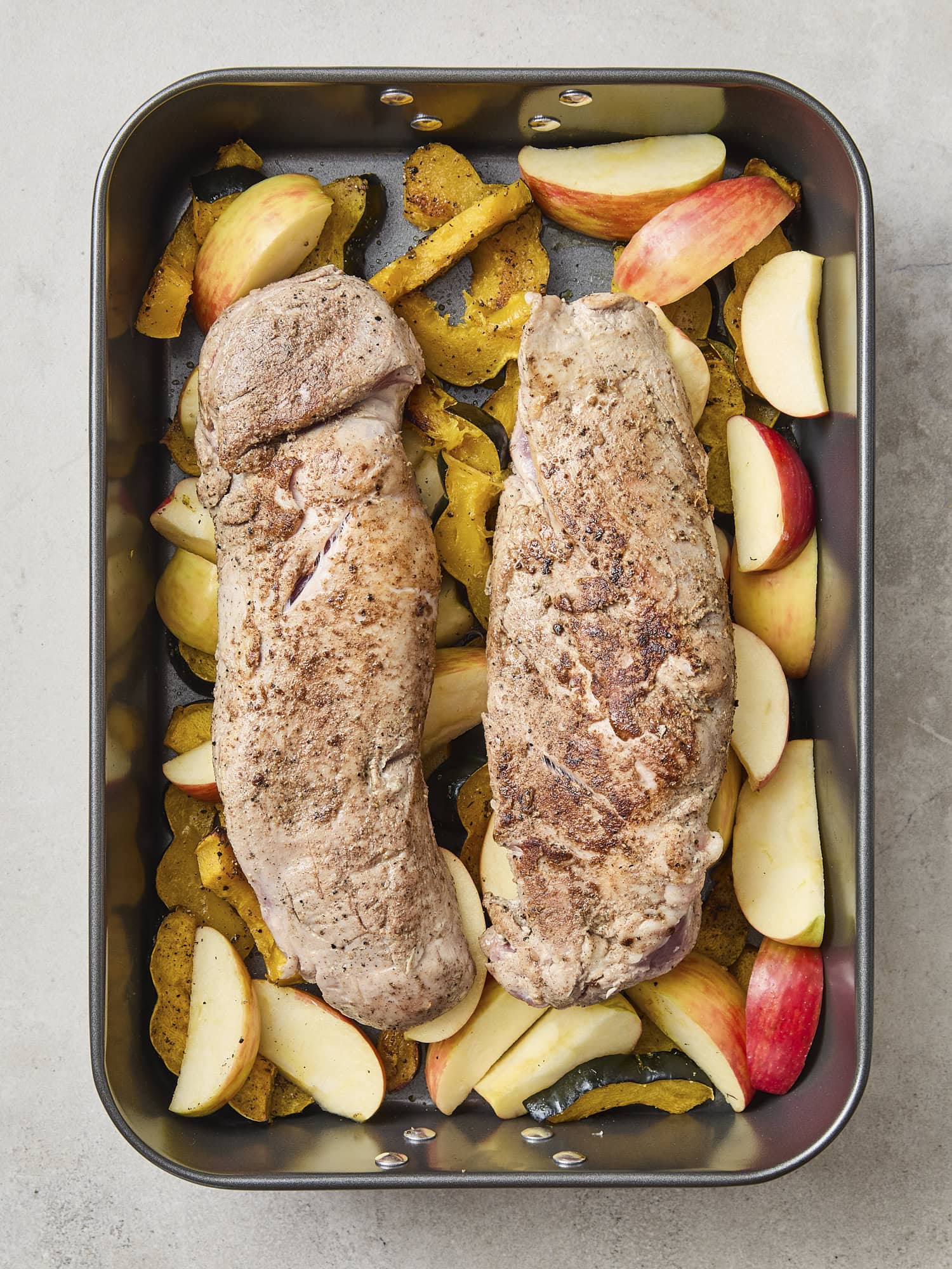Pork tenderloin before roasting with apples and squash underneath.