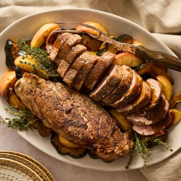 Platter with two pork tenderloins with apples and squash sliced around.